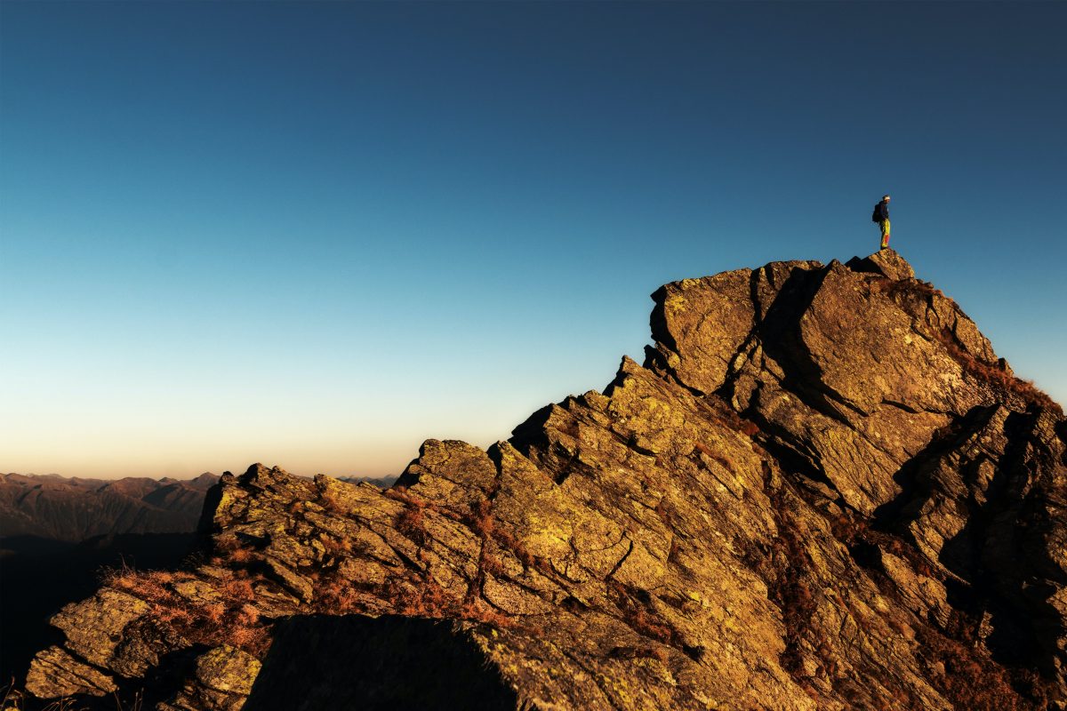 Photo of a hiker standing on the top of a rocky mountain top.