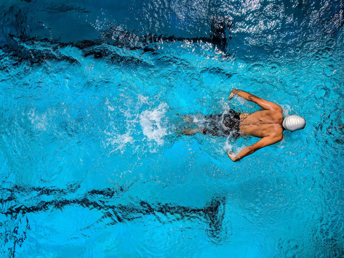A view from above a man swimming with a swim cap on in a large pool.