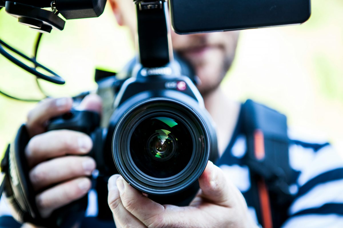A man's face is visible behind a camera lens.