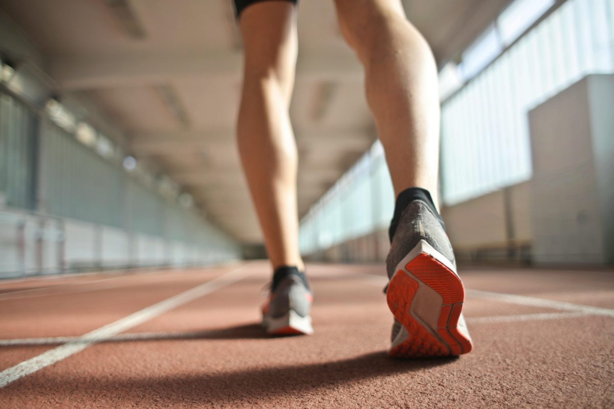 A photo of a runner on a track. The runner has a light skin tone and is wearing black socks and gray sneakers. The runner is shown only from the knees down.