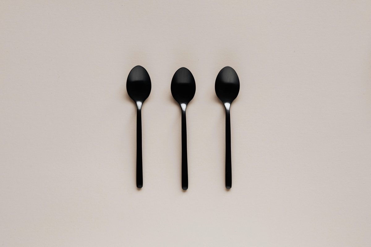 Three shiny black spoons are placed in a row on a light beige background.