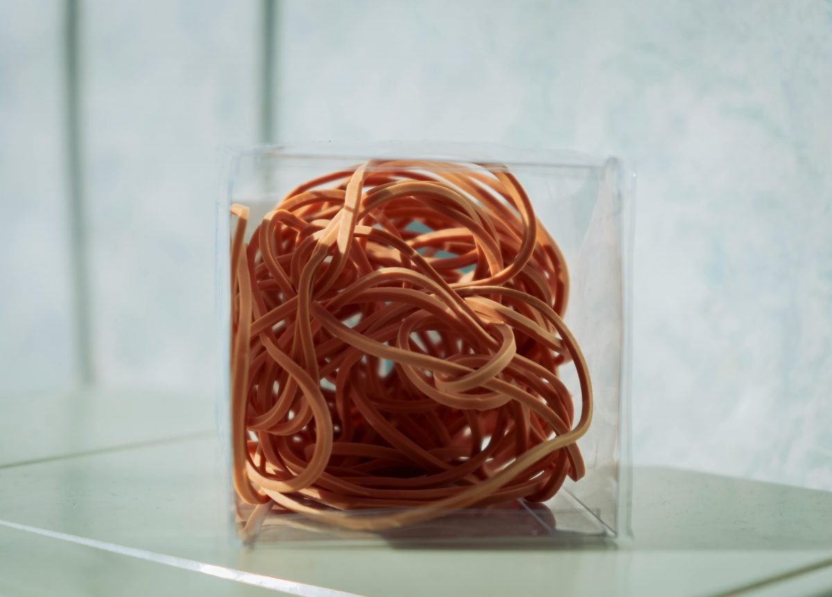 A clear box full of orange elastic bands sits on a table.