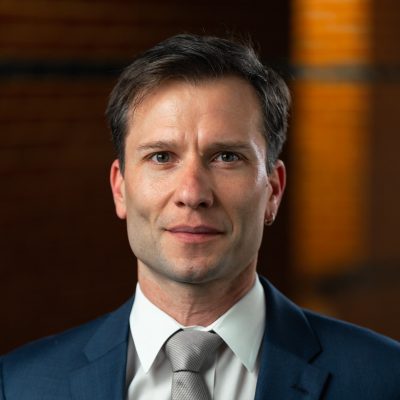 Portrait of Prof. Kay Wille. He has short, brown hair, light skin, and is wearing a blue suit jacket, white collared shirt and a silver tie.